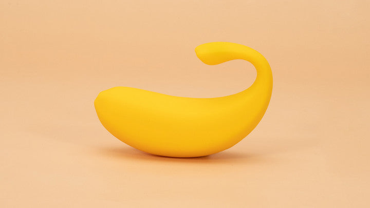 A yellow banana-shaped object with a curved tip, set against a light peach background.